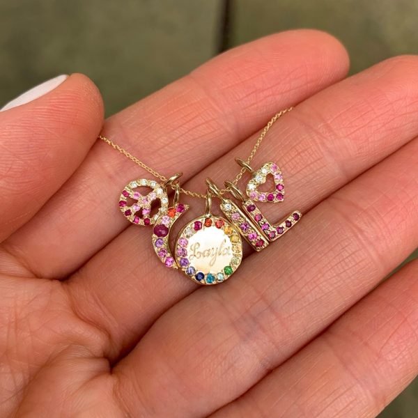 holding-charms-in-hand-for-size-perspective Mini Charm Jewels - Size guide for size of the charms - holding gold peace charm, gold moon charm, gold circle charm, gold skinny bar charm, gold letter charm and heart charms with personalized gemstones
