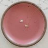 14k gold egg charm necklace and sterling silver egg charm on a pink plate