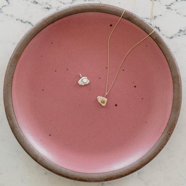 14k gold egg charm necklace and sterling silver egg charm on a pink plate