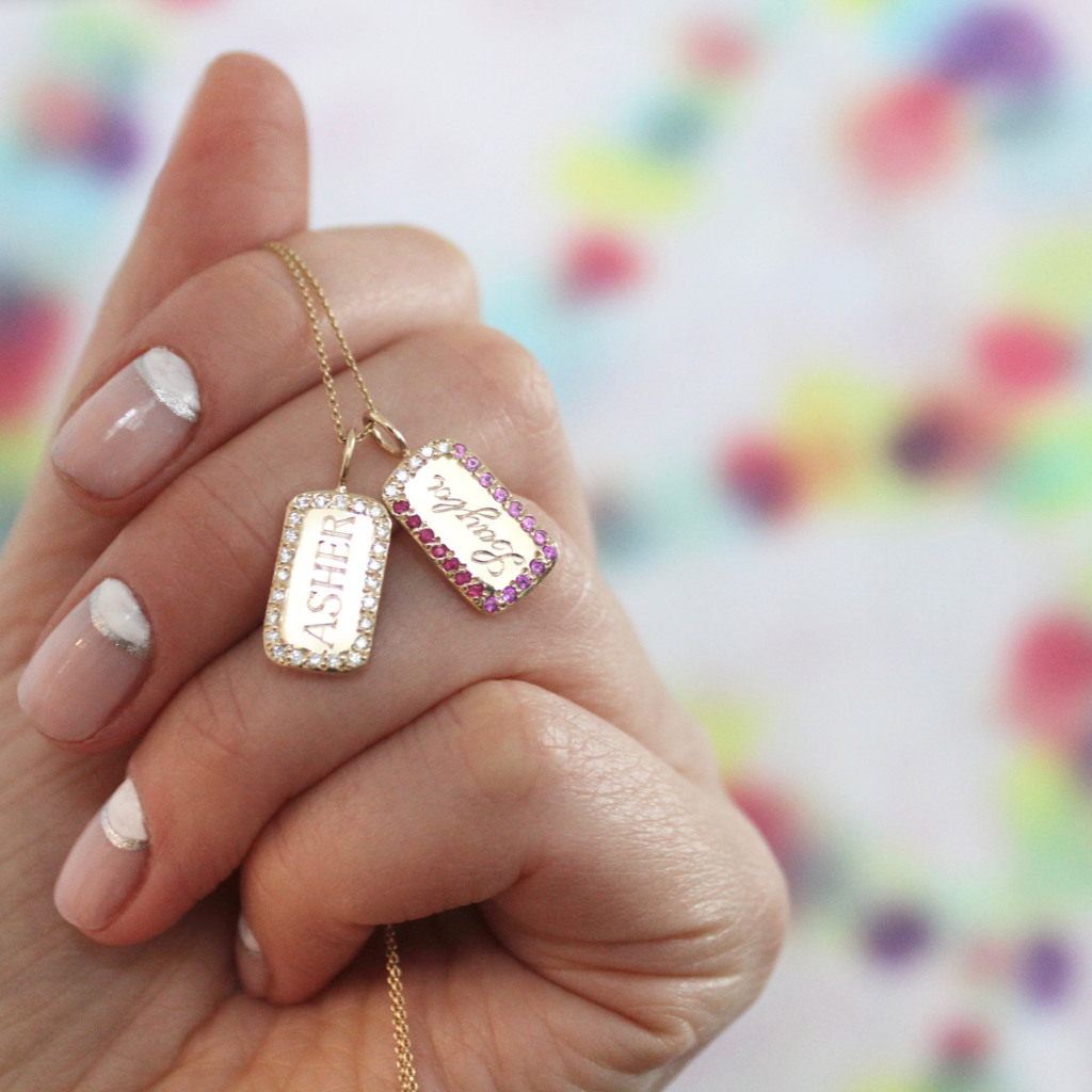 hand holding the Classic ID Tablet Charms on a necklace one with diamonds and one with pink hues