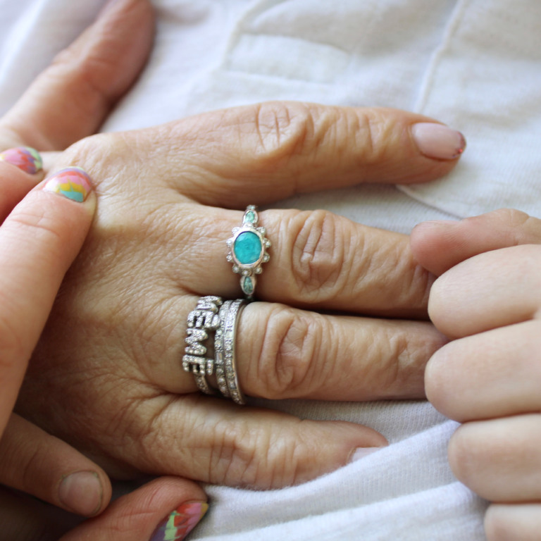 Close-up holding Grandma's hand wearing the new grandma wearing the new paraiba tourmaline flower ring and other rings