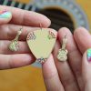 Holding the new rainbow colored gemstone 14k yellow gold guitar charm, the rainbow colored 14k yellow gold guitar pick charm, and another 14k yellow gold guitar charm with white diamonds