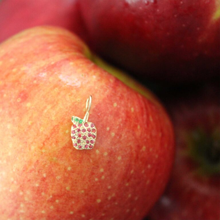 gold apple charm with red ruby gemstones on top of a ruby red apple