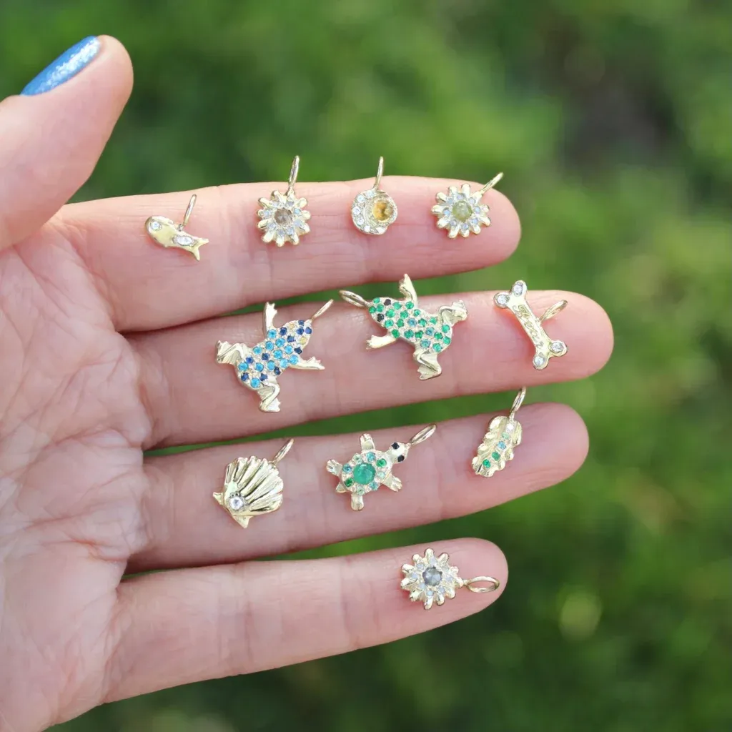 different nature themed gold charms with gemstones and diamond held up close with a green natural background