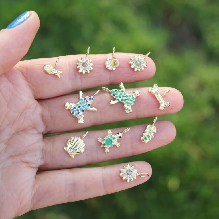 different nature themed gold charms with gemstones and diamond held up close with a green natural background