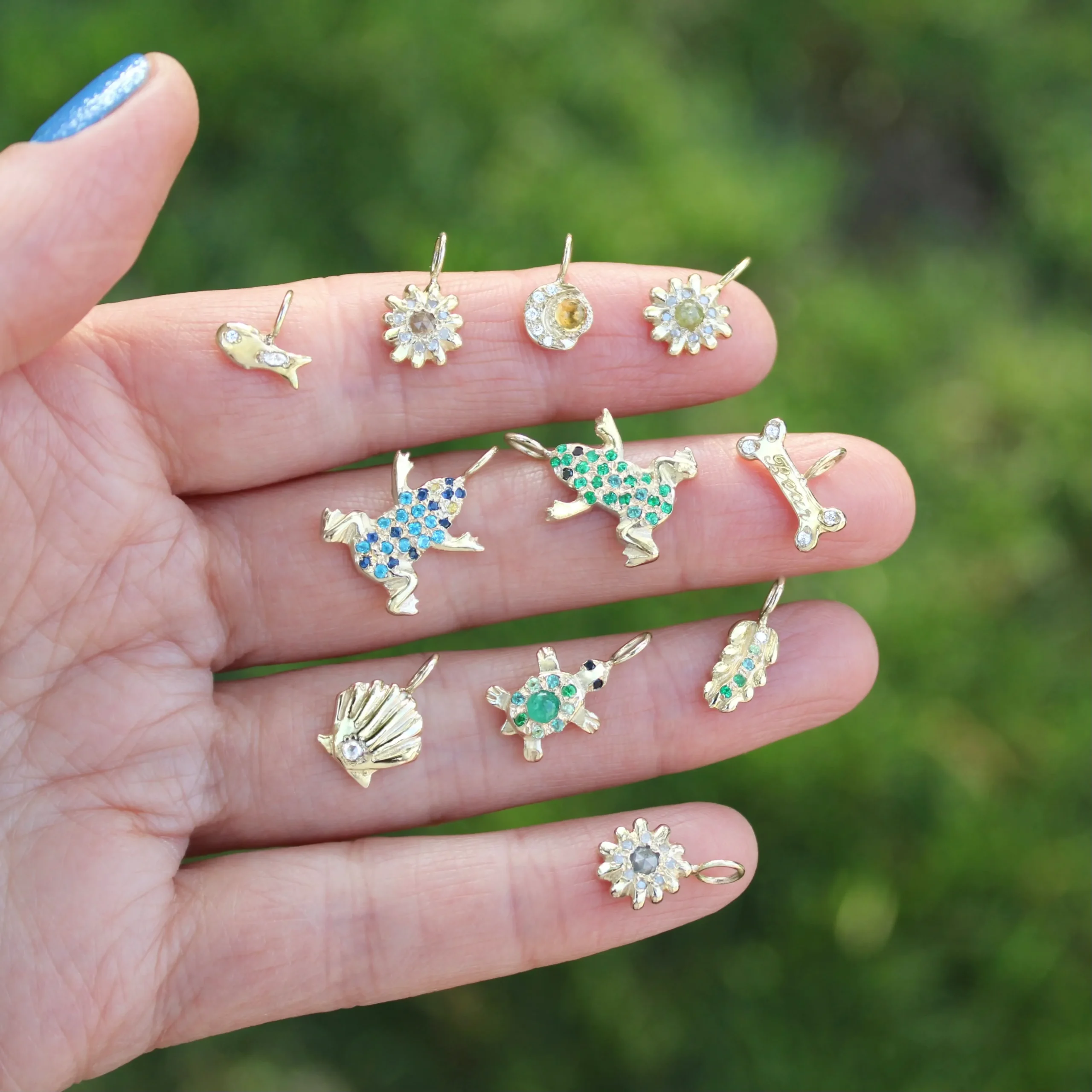 different nature themed gold charms with gemstones and diamond held up close with a green natural background